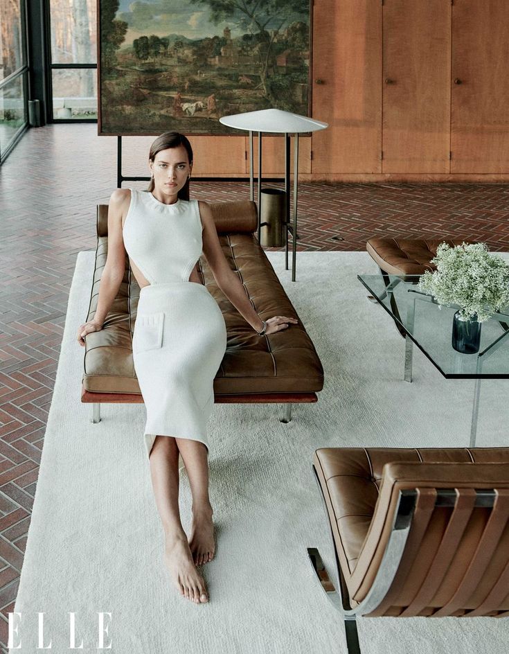 a woman in a white dress is sitting on a couch and looking at the camera