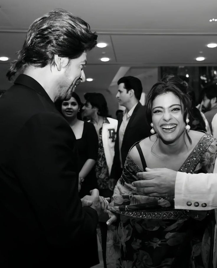 a man in a suit talking to a woman at a party with other people standing around