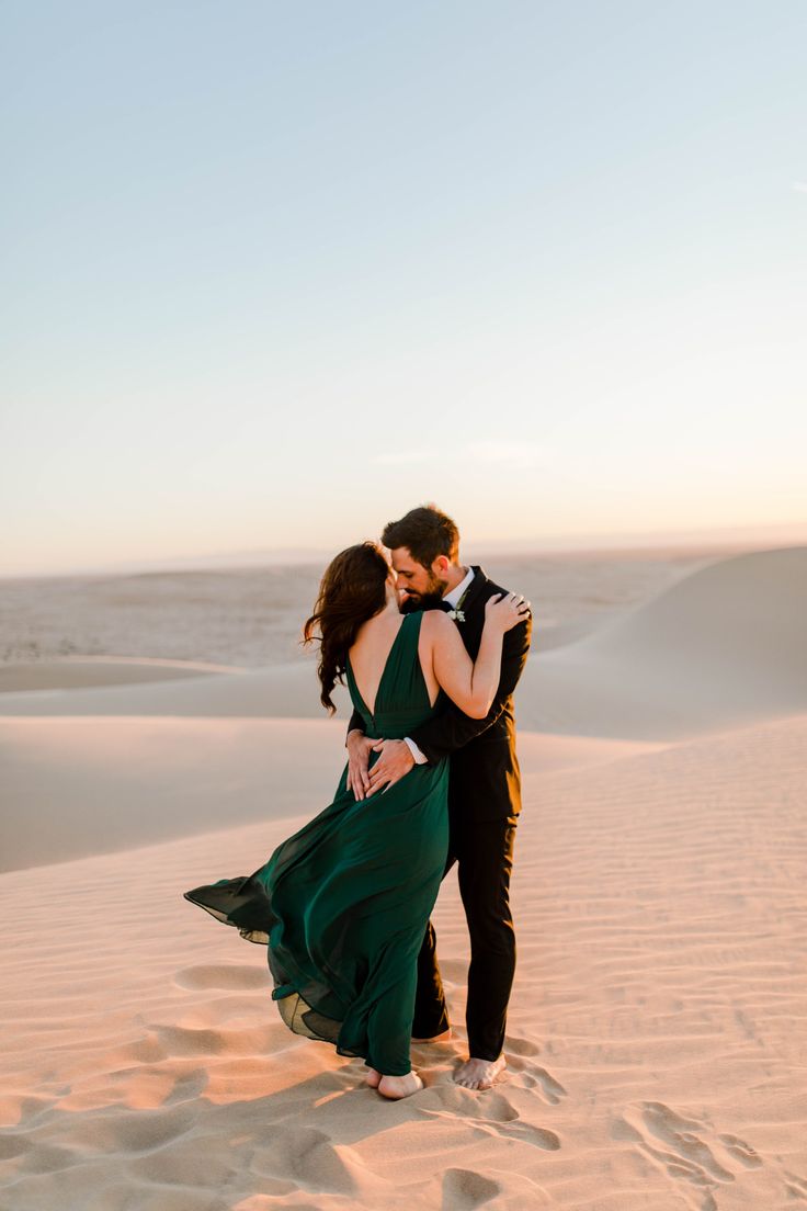 a man and woman embracing in the sand dunes at sunset, with their arms around each other