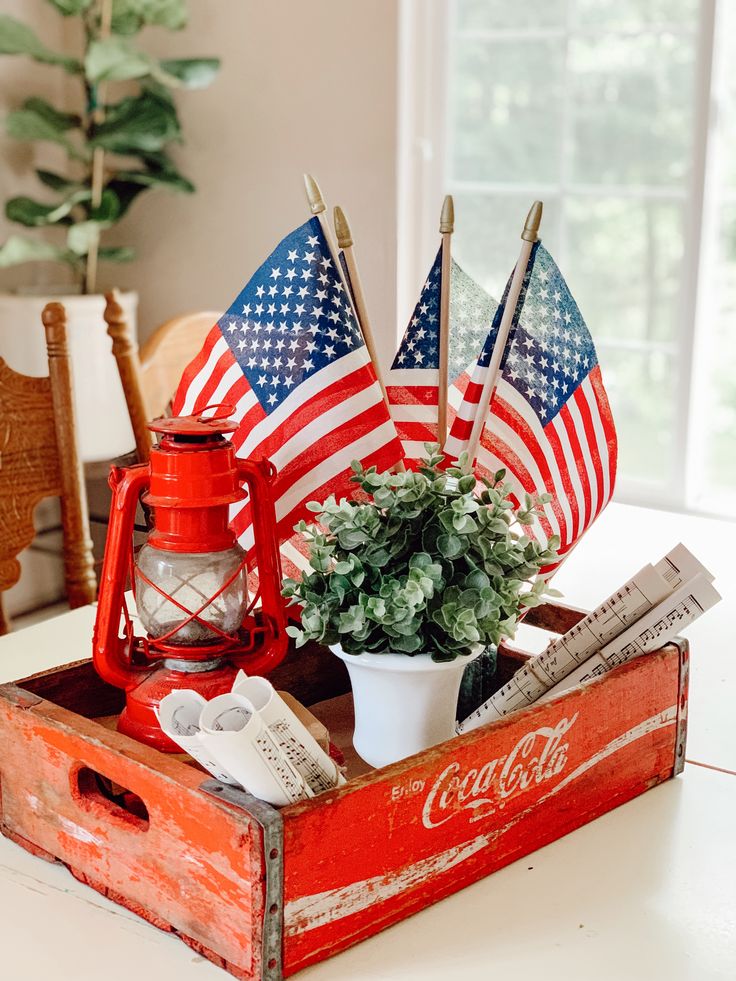 an old coca - cola crate filled with american flags and other patriotic items sits on a dining room table