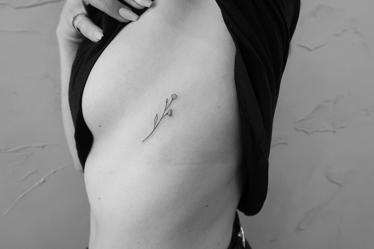 a woman with a small flower tattoo on her left side ribcage, showing it's thinness