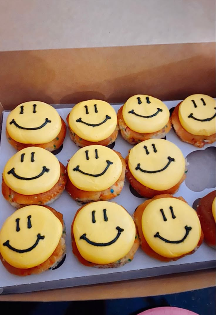 a box filled with lots of yellow cupcakes covered in frosting and smiling faces