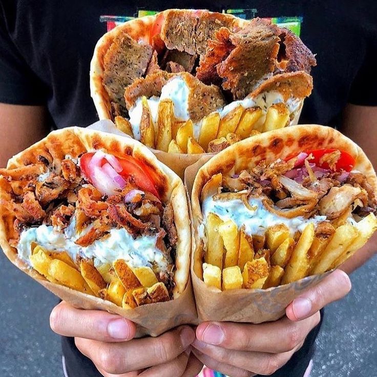 three pita sandwiches with french fries and ketchup on the side, in front of a man