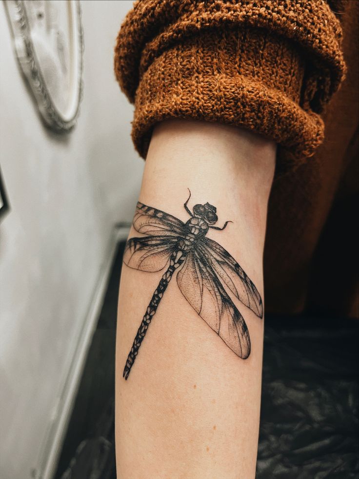 a woman's arm with a dragonfly tattoo on it