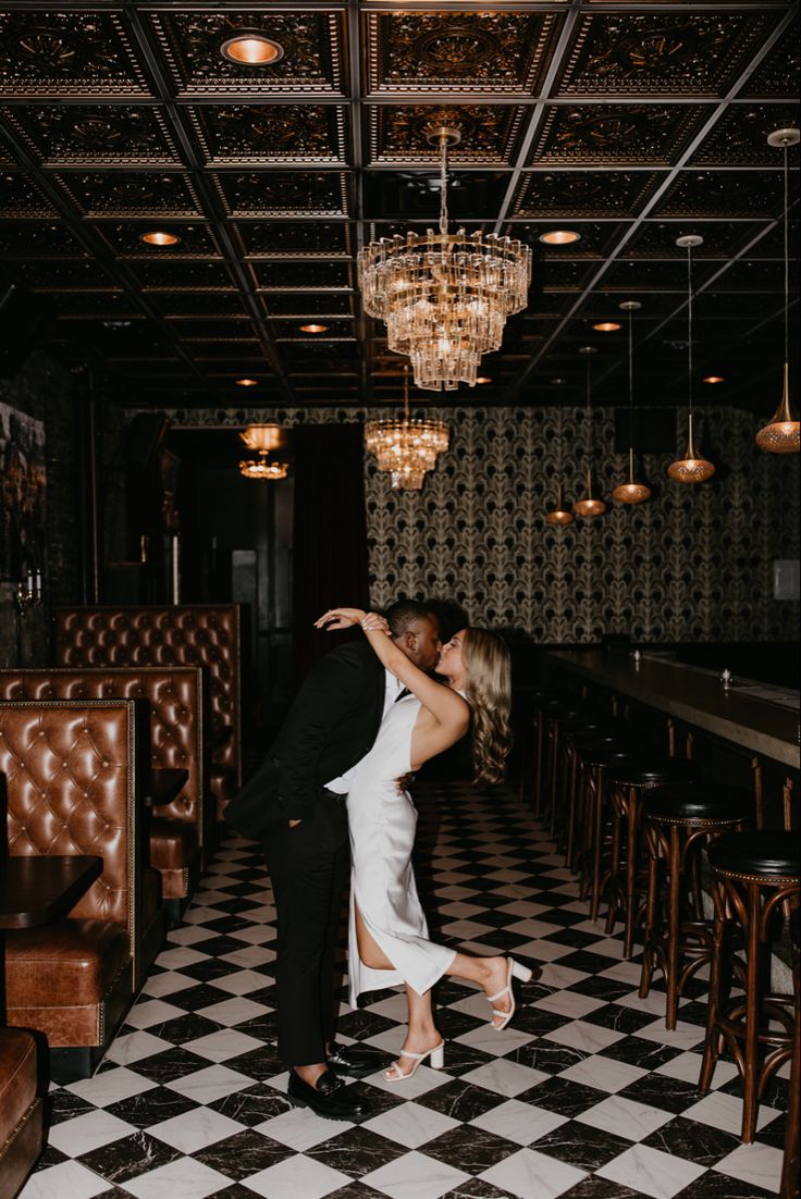 a bride and groom kissing in the middle of a room with black and white checkered floor