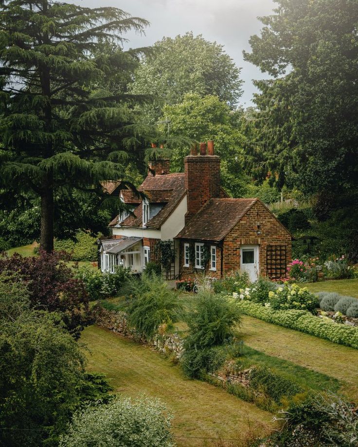 a house surrounded by trees and flowers in the middle of a lush green park area