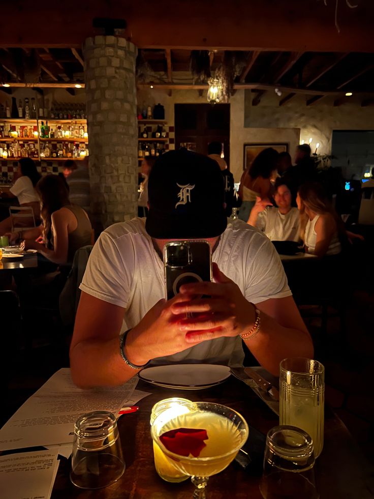 a man sitting at a table taking a selfie with his cell phone in front of him