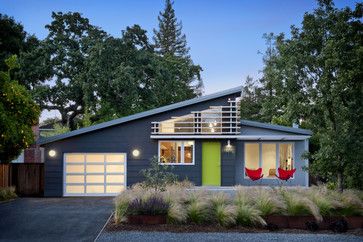 a modern house with green door and two red chairs in the front yard at dusk