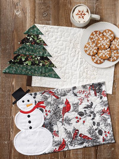 a wooden table topped with christmas themed napkins next to a plate of cookies and a cup of coffee