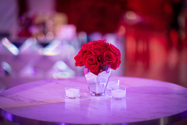 red roses in a vase on a table with ice cubes and candlelight background