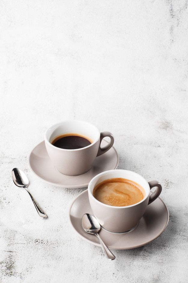 two cups of coffee on saucers with spoons next to each other and one is empty