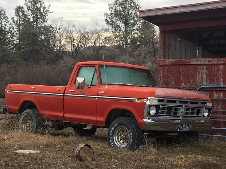 an old red pick up truck parked in front of a barn