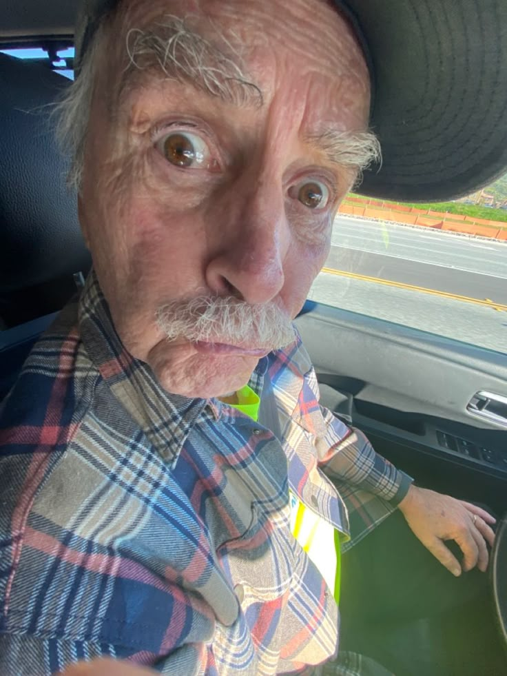 an old man with a hat and plaid shirt in the back seat of a car