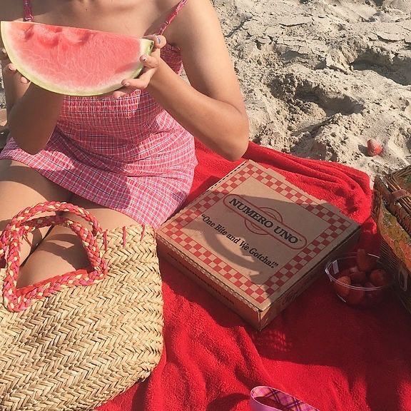 a woman sitting on the beach eating a piece of watermelon next to her purse