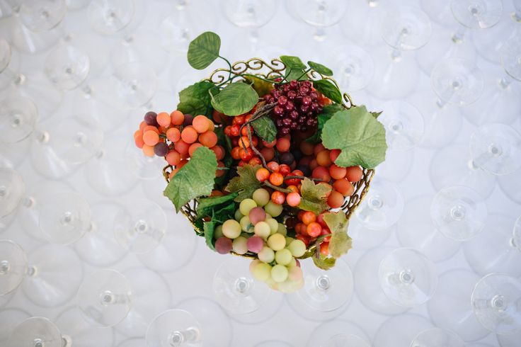 a bunch of grapes and other fruits on a white surface with wine glasses in the background