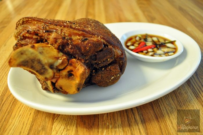 a white plate topped with meat next to a bowl of dipping sauce on top of a wooden table