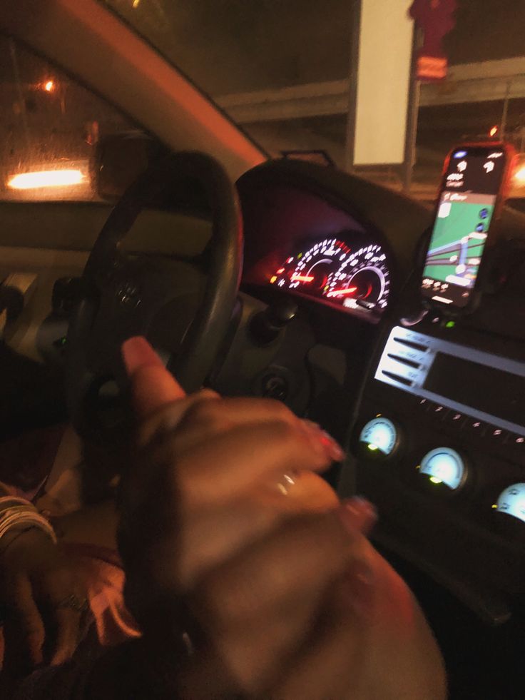 a person driving a car with their hand on the steering wheel and pointing to the dashboard