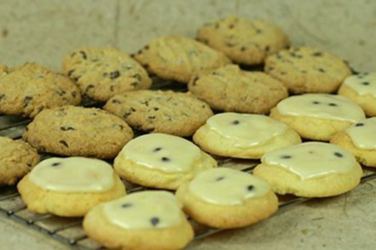 cookies with white icing and chocolate chips are cooling on a rack in the kitchen