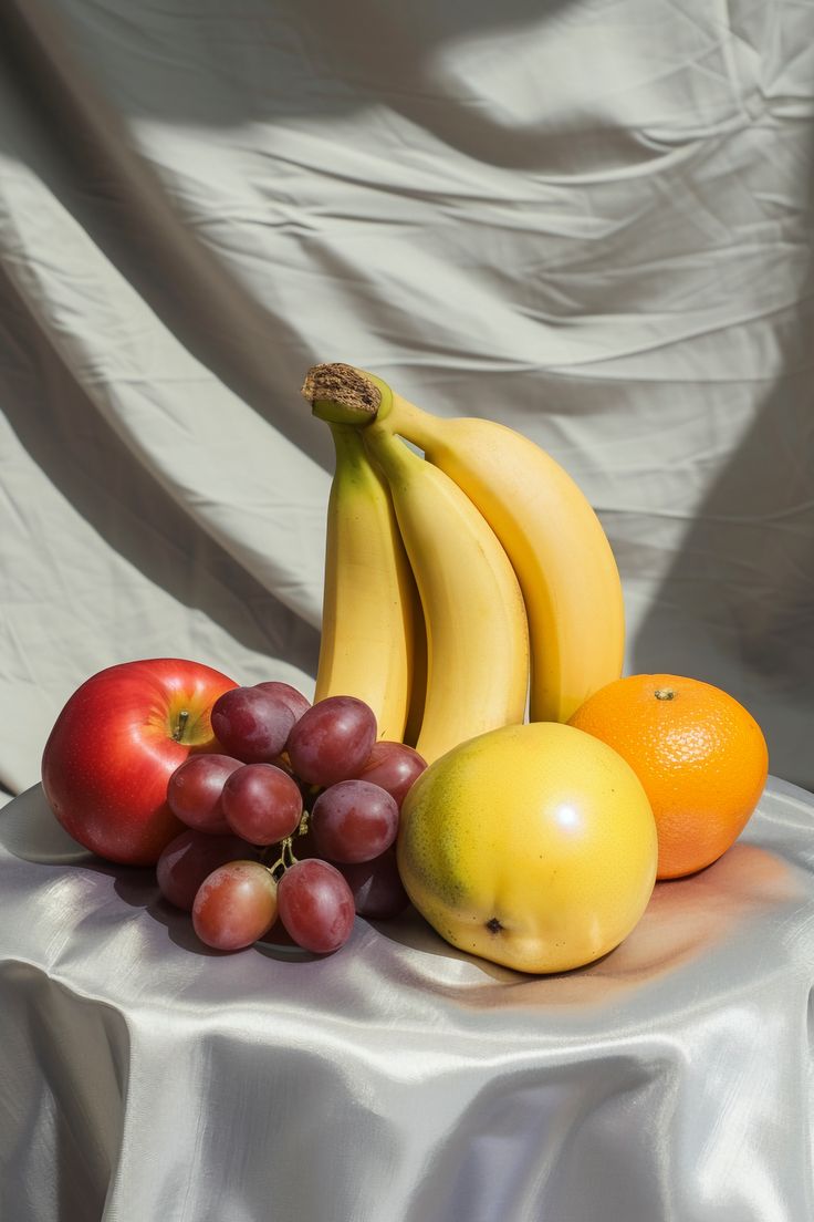 a bunch of fruit sitting on top of a white table cloth covered table with a curtain behind it