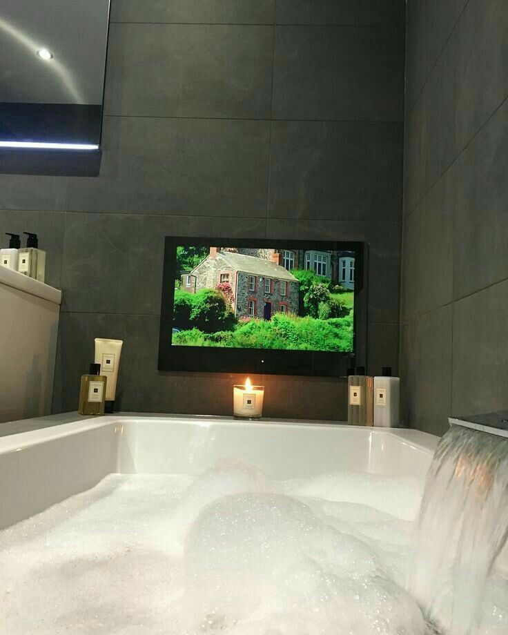 a bathroom with a large tv on the wall next to a bathtub filled with water