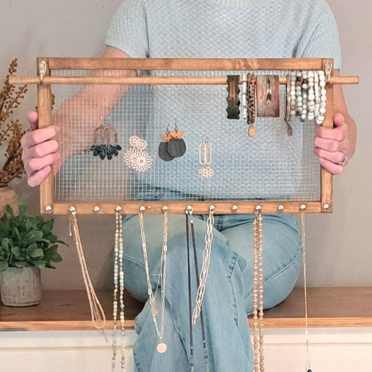 a person sitting on a shelf holding up a wooden frame with jewelry hanging from it