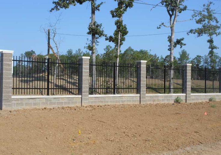 a fenced in area with concrete blocks and black iron fences on the side of it