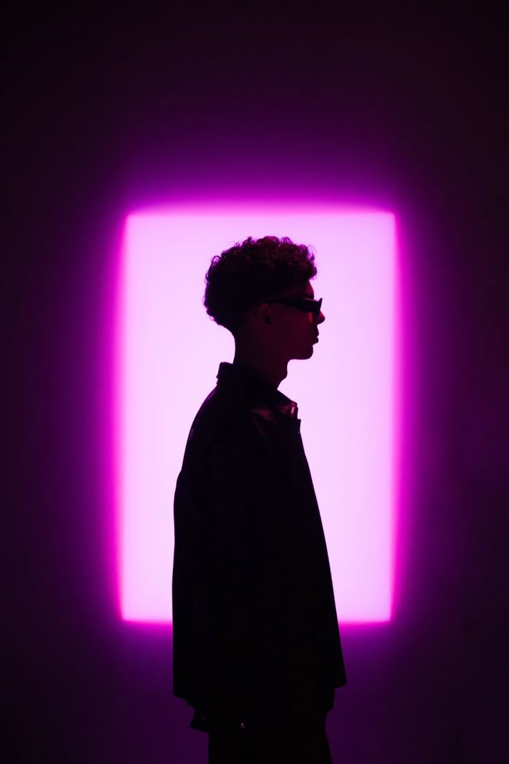 a man standing in front of a purple light with his head turned to the side