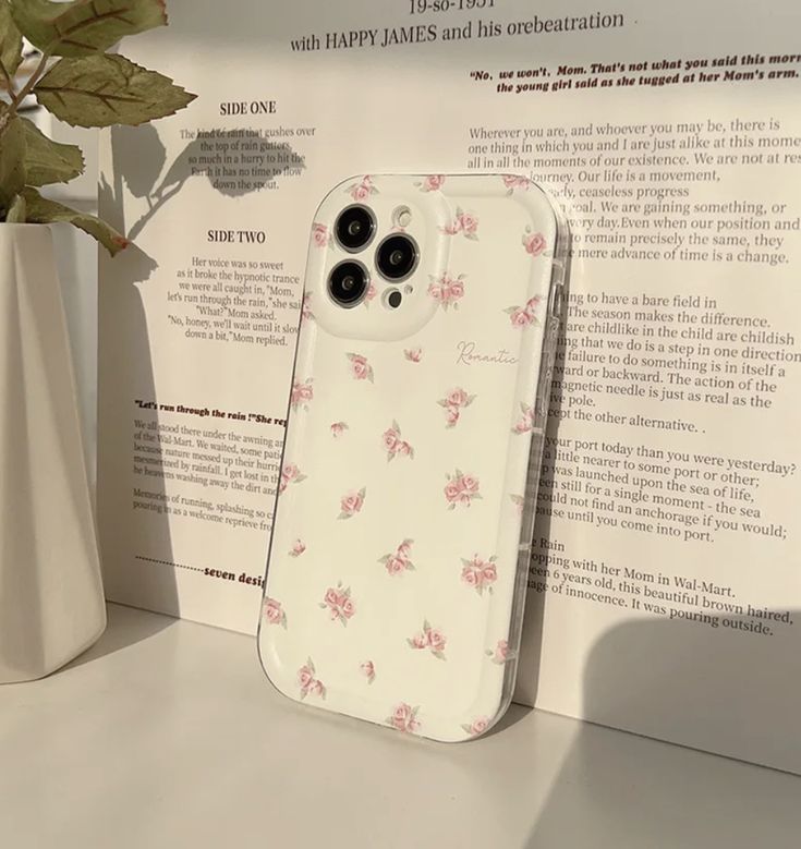 an iphone case sitting on top of a table next to a vase with flowers in it