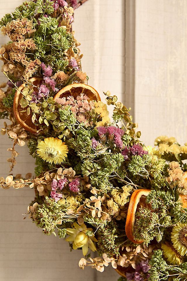 an arrangement of dried flowers and oranges in a vase