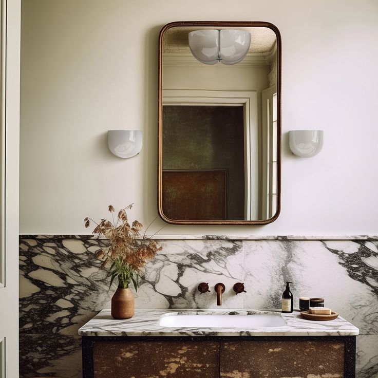 a bathroom with marble counter top and mirror above the sink, along with two vases filled with flowers