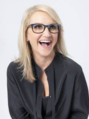 a woman with glasses and a black shirt smiling at the camera in front of a white background