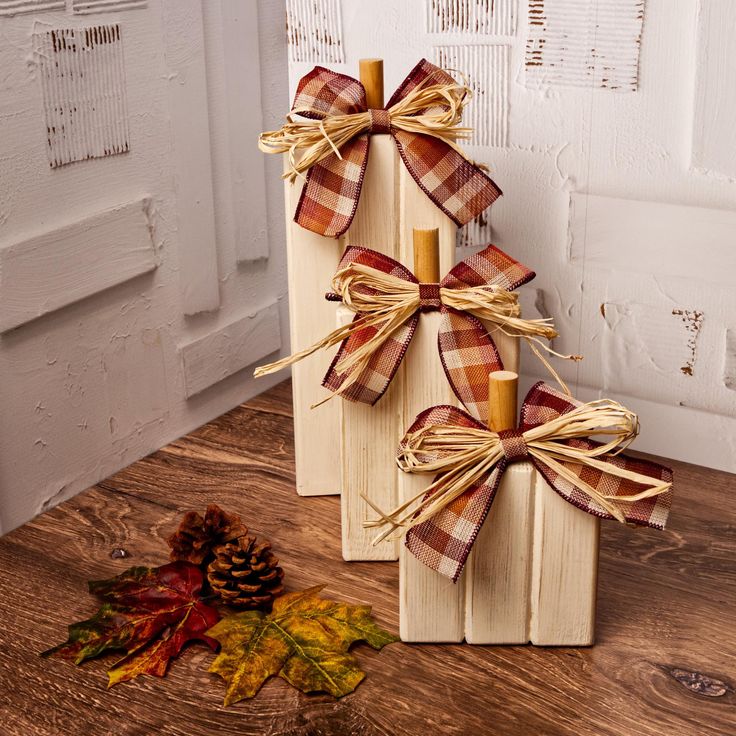 two wooden blocks with bows on them sitting next to a pine cone and fall leaves