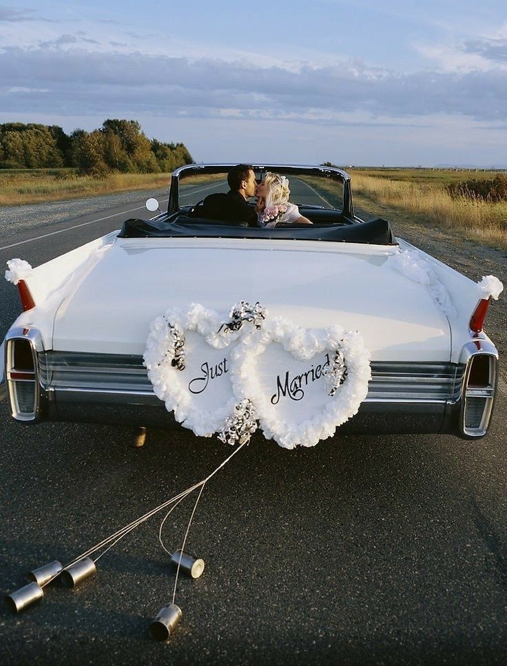 a bride and groom kissing in the back of a white convertible car decorated for their wedding