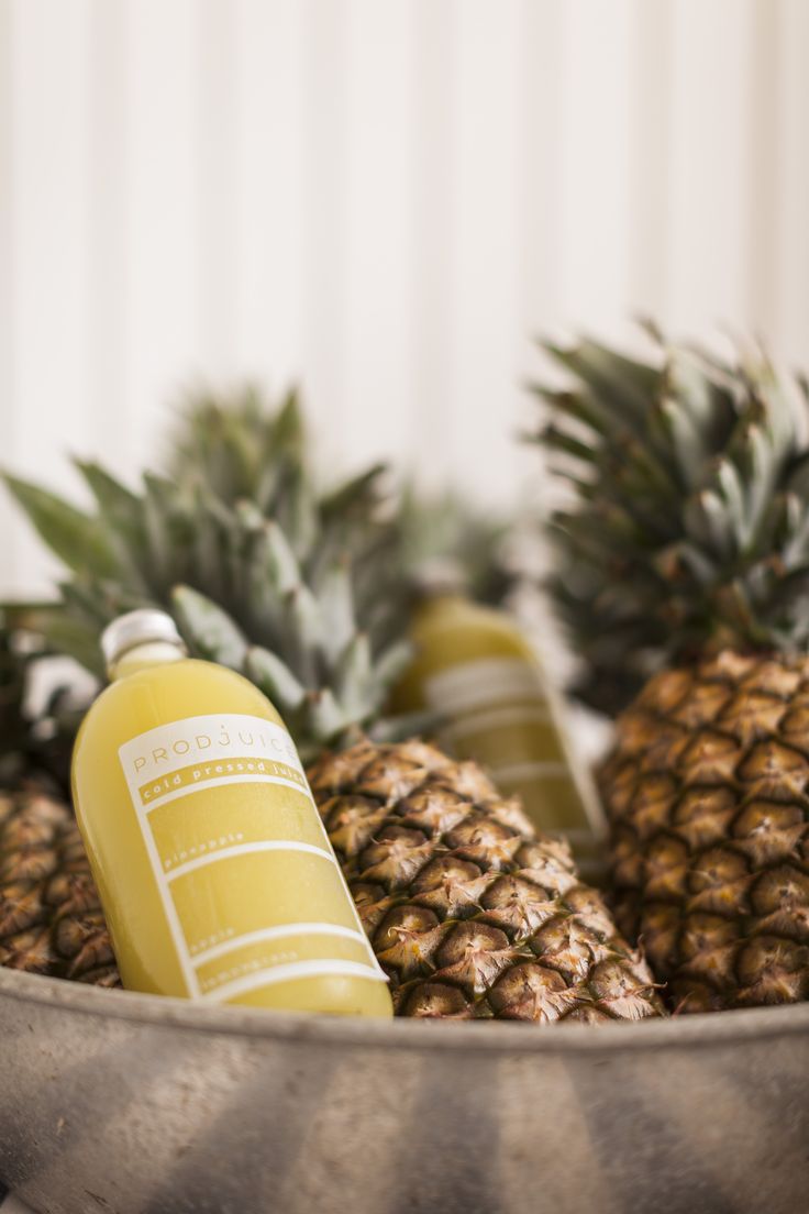 several pineapples and two bottles of juice in a metal bowl on a table