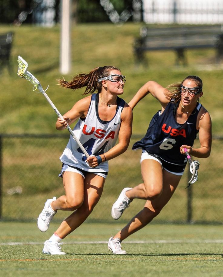 two girls playing field hockey on the field with one running after the ball and the other trying to block it