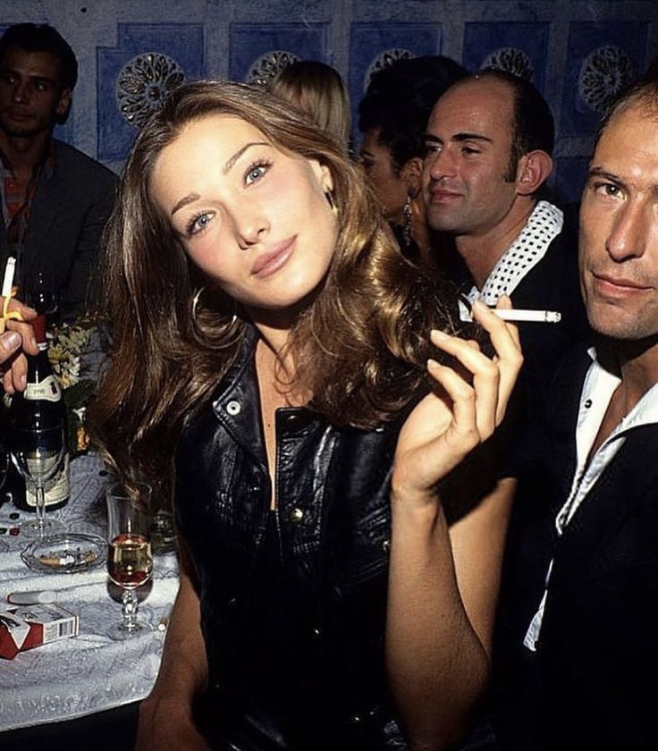 two men and a woman sitting at a table with drinks in front of their faces