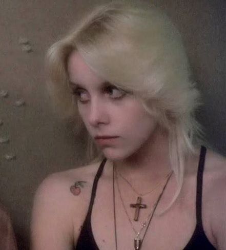 a woman with blonde hair wearing a black tank top and cross pendants on her neck