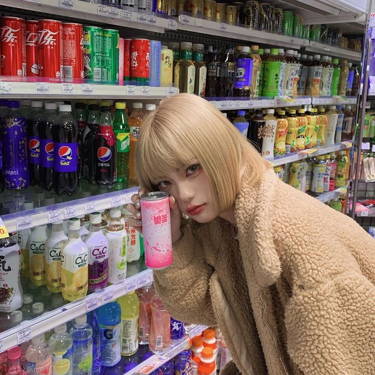 a woman holding a cup in front of a store shelf filled with drinks and sodas