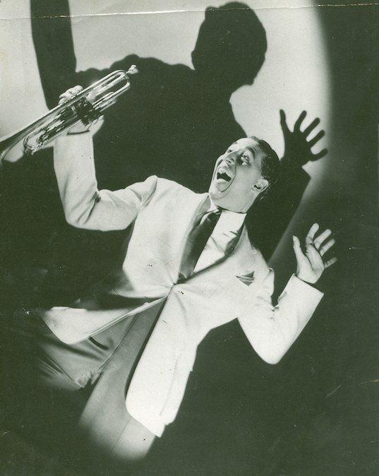 a man in a suit and tie holding a trumpet up to his face while standing next to a shadow