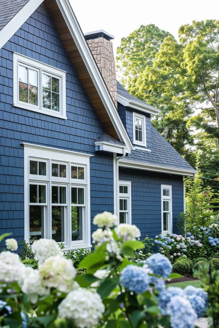 a blue house with white windows and flowers in the foreground on a sunny day