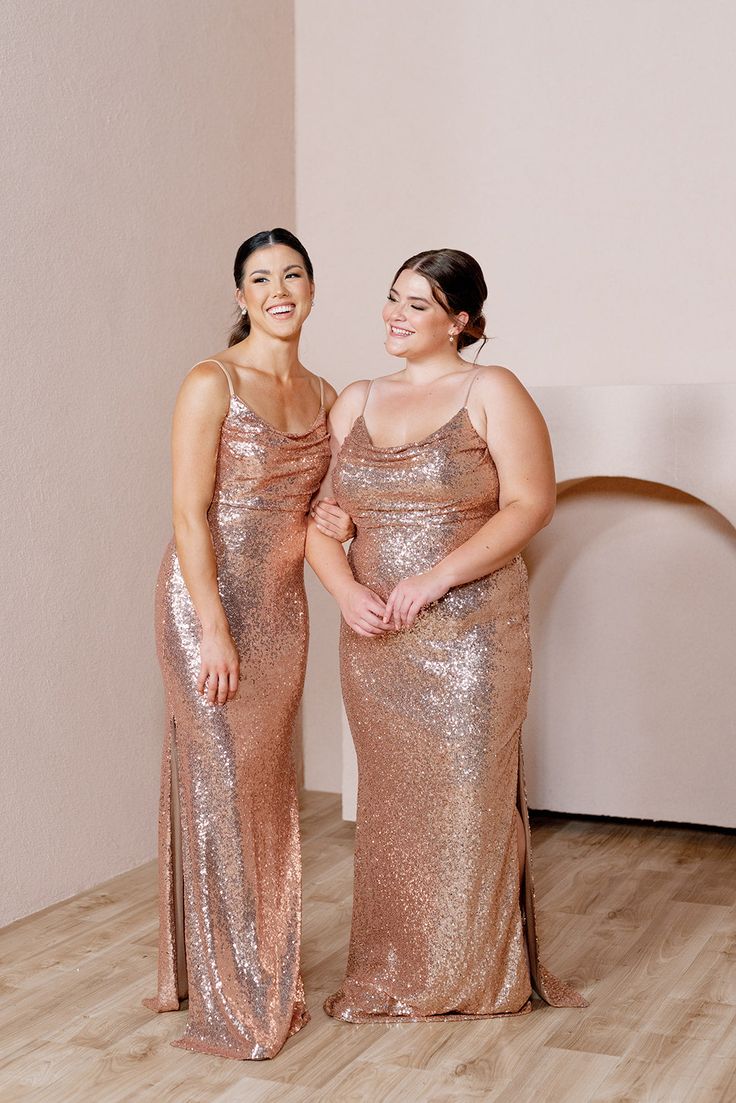 two women standing next to each other in gold sequin gowns smiling at the camera