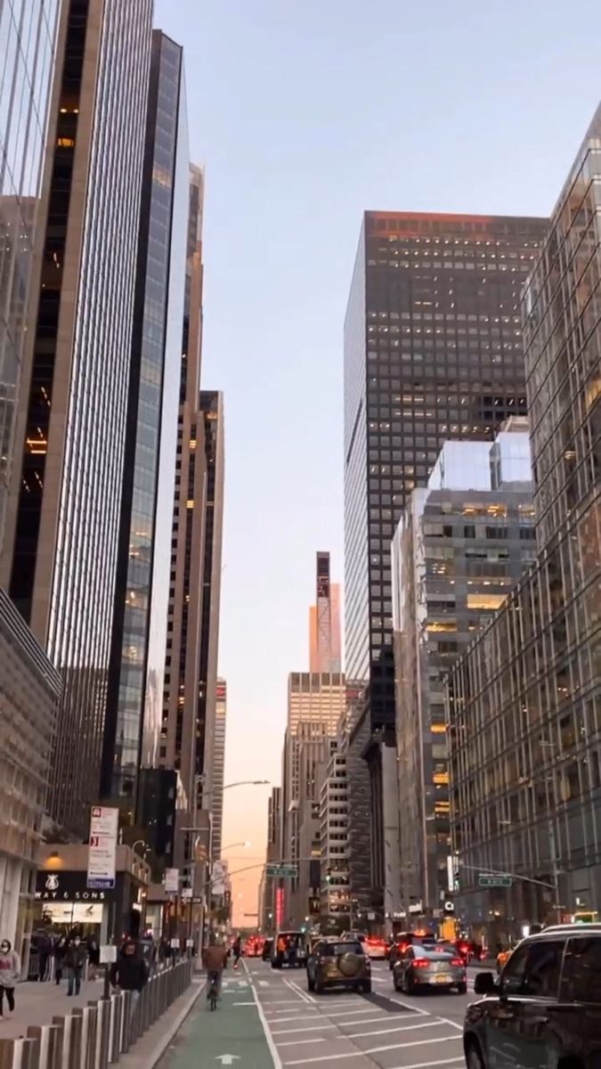 a city street filled with lots of tall buildings next to traffic and people walking on the sidewalk