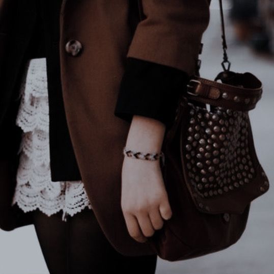 a woman carrying a brown purse while walking down the street with her hand on her hip