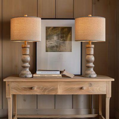 two lamps sitting on top of a wooden table next to a framed photograph and books