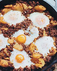 three fried eggs are on top of some meat in a skillet with other food items