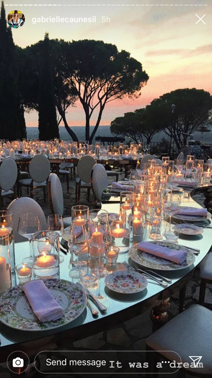 a table set up with candles and plates on it for an outdoor dinner party at dusk