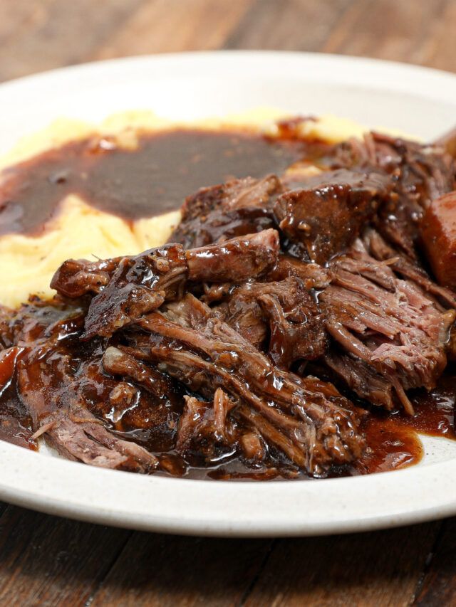 a white plate topped with meat and gravy on top of mashed potatoes