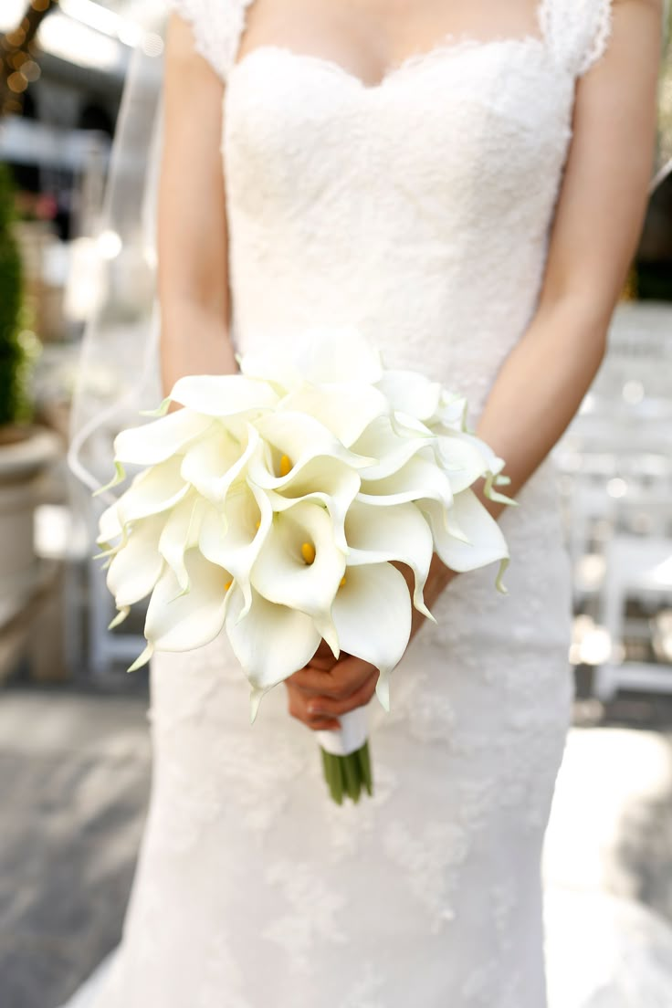 a woman in a wedding dress holding a bouquet of white flowers on her left hand