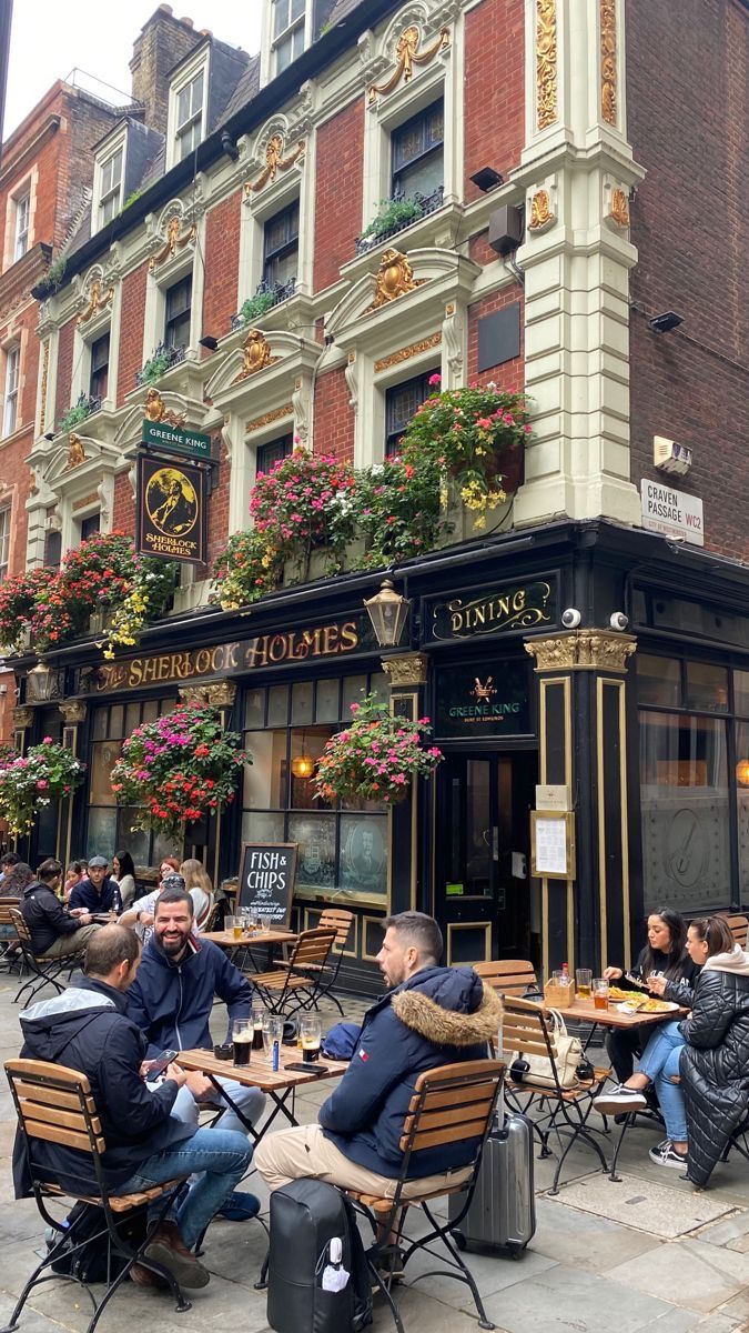 people sitting at tables in front of a building with flowers growing on the side of it