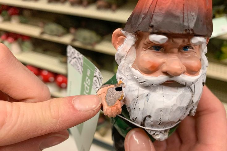 a hand holding a small gnome figurine in a store